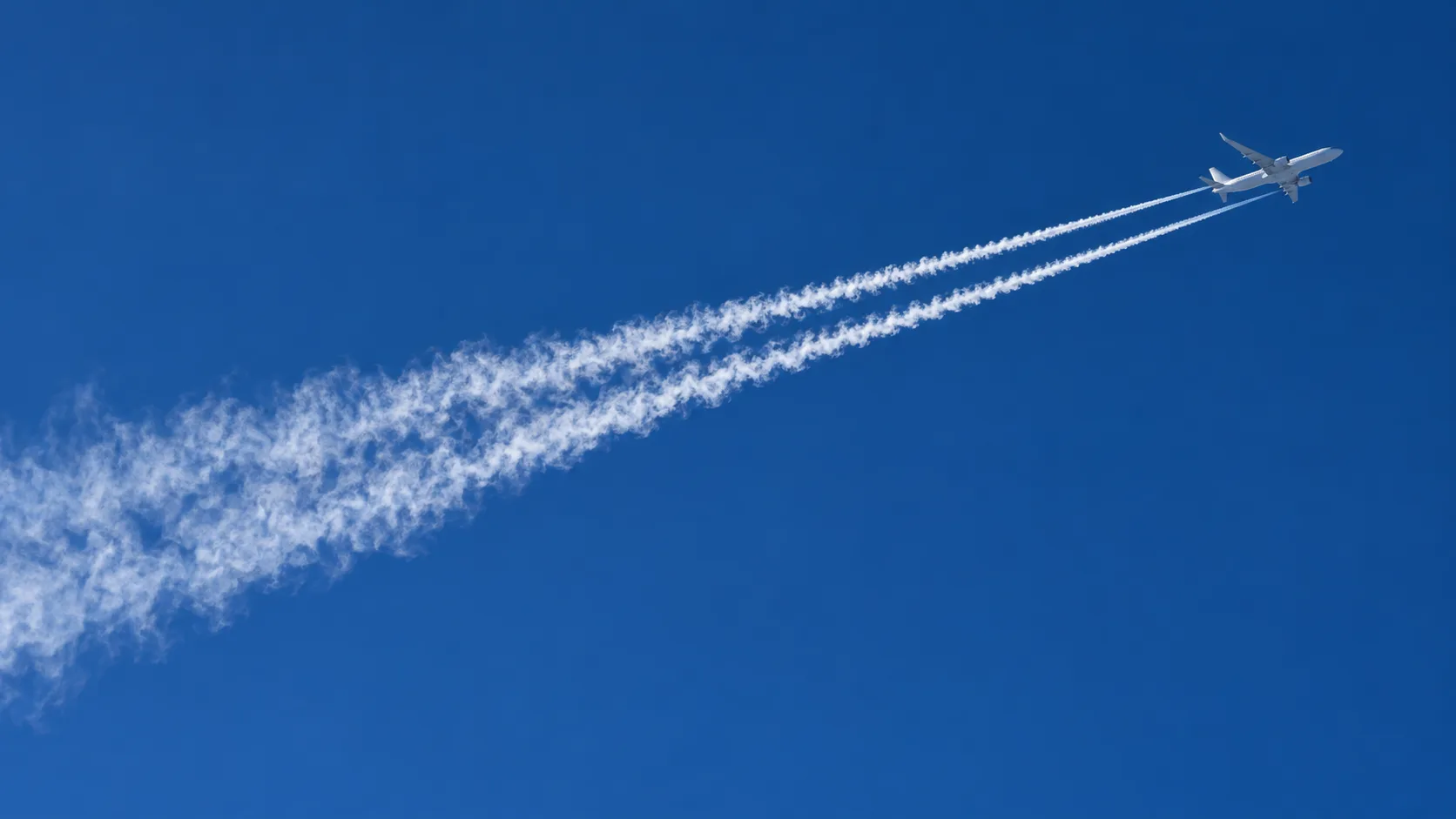 藍天中一架客機身後拖着兩道白色尾跡，遠端的白線逐漸擴散